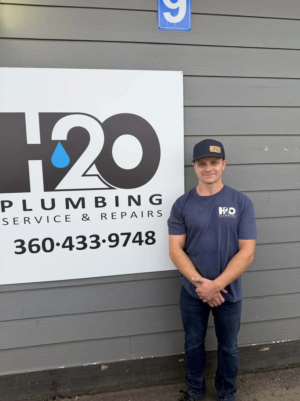 H2O crew member in a navy shirt beside the H2O Plumbing sign